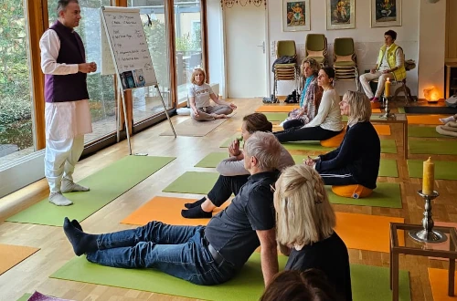 Auf Yogamatten sitzende Menschen mit Lehrer am linken Bildschirmrand
